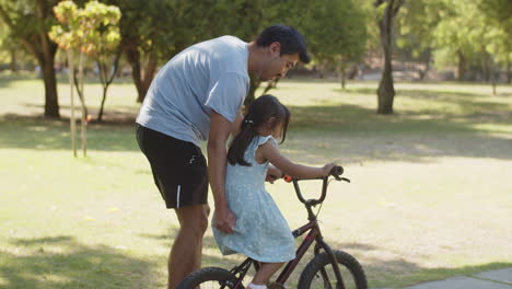 Hombre-Asiático-Feliz-Enseñando-A-Su-Pequeña-Hija-A-Andar-En-Bicicleta
