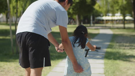 Rückansicht-Des-Vaters,-Der-Seiner-Tochter-Das-Fahrradfahren-Im-Park-Beibringt