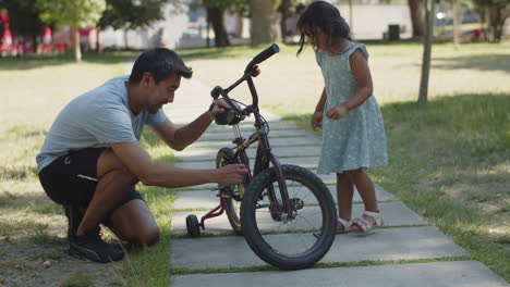 Glücklicher-Vater,-Der-Die-Kette-Am-Fahrrad-Seiner-Kleinen-Tochter-Anpasst