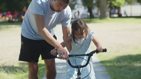 Joven-Padre-Asiático-Enseñando-A-Su-Hija-A-Andar-En-Bicicleta-En-El-Parque