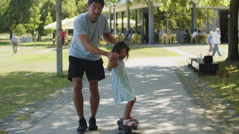 Happy-Asian-father-holding-little-daughter-during-skate-ride
