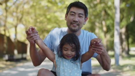 Glücklicher-Asiatischer-Vater-Und-Tochter,-Die-Mit-Ausgestreckten-Armen-Sitzen-Und-Sich-Bewegen