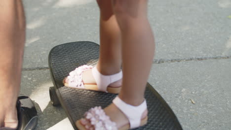 Close-up-of-legs-of-little-girl-standing-on-skateboard-outdoors