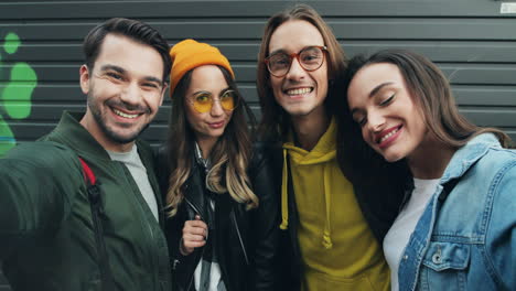 Close-up-view-of-group-of-caucasian-funny-friends-in-hipster-style-smiling-and-posing-while-taking-selfies-in-the-street