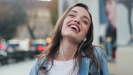 Close-up-view-of-young-Caucasian-woman-in-headphones-listening-to-the-music-on-smartphone,-singing-and-dancing-in-the-street-while-looking-at-the-camera