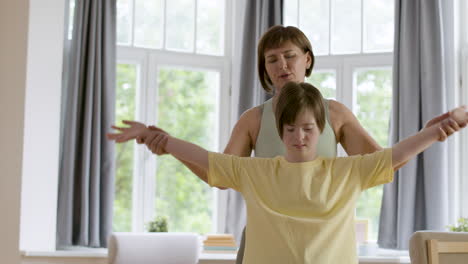Woman-holding-hands-of-her-down-syndrome-daughter-for-teaching-her-a-yoga-posture