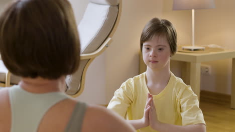 Young-girl-with-down-syndrome-imitating-her-mother-doing-yoga-posture-at-home