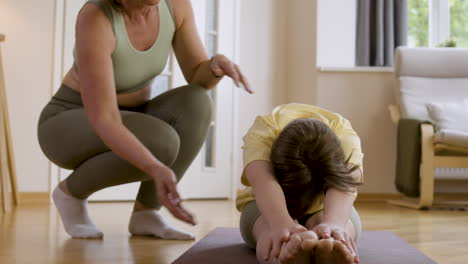 Young-girl-stretching-on-yoga-mat-with-the-help-of-her-trainer