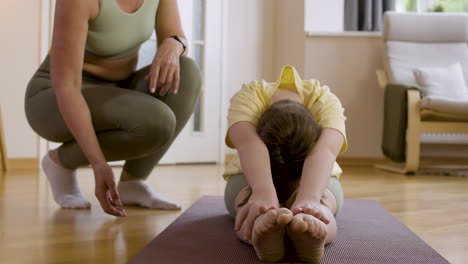 Woman-helping-girl-with-flexibility-at-home