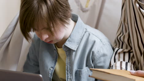 Closeup-of-young-gir-with-down-syndrome-using-laptop-next-to-woman-with-book