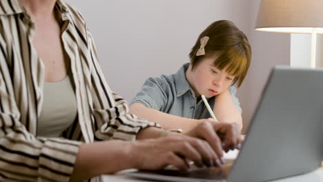 Closeup-of-woman-working-on-laptop-and-her-daughter-doing-homework-next-to-her