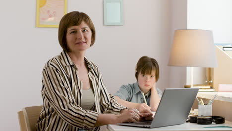 Woman-looking-at-camera-while-her-daughter-studies