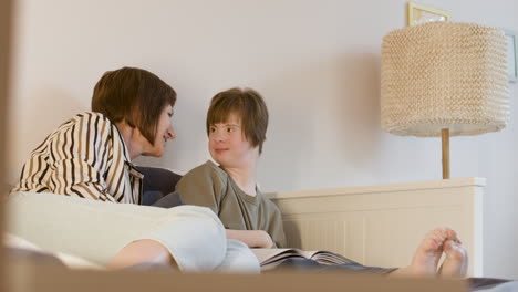 Young-girl-with-down-syndrome-reading-magazine-and-her-mother-is-kissing-her