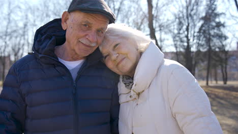 Seniorenpaar-Umarmt-Und-Schaut-An-Einem-Wintertag-Im-Park-In-Die-Kamera