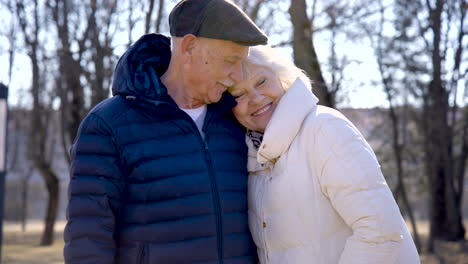 Camera-zooming-of-a-senior-couple-who-is-hugging-and-looking-at-camera-in-the-park-on-a-winter-day