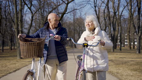 Senior-couple-holding-bikes-while-walking-and-talking-in-the-park-on-a-winter-day
