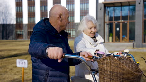 Side-view-of-a-senior-couple-holding-bikes-while-walking-and-talking-in-the-park-on-a-winter-day