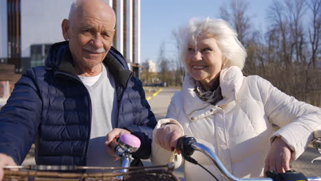 Älteres-Paar,-Das-Fahrräder-Hält,-Während-Es-An-Einem-Wintertag-In-Die-Kamera-Schaut-Und-Im-Park-Lächelt