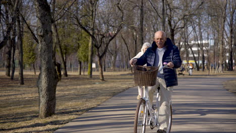 Front-view-of-a-senior-couple-riding-bikes-in-the-park-on-a-winter-day