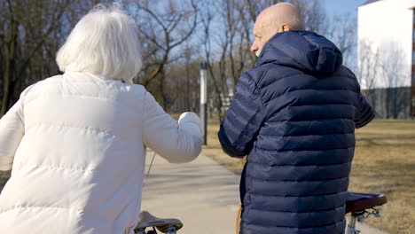 Rückansicht-Eines-älteren-Paares,-Das-Fahrräder-Hält,-Während-Es-An-Einem-Wintertag-Im-Park-Spazieren-Geht-Und-Spricht