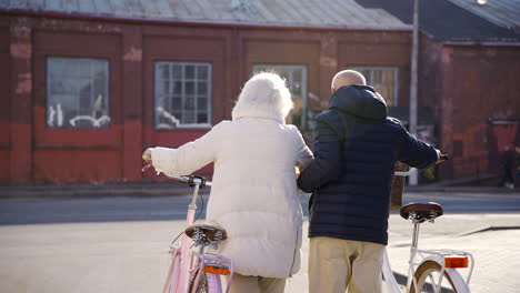 Rear-view-of-a-senior-couple-walking-while-holding-bikes-in-the-street-on-a-winter-day