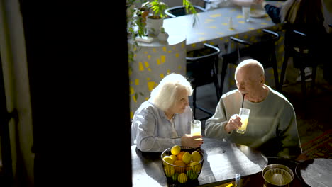 Top-view-of-a-senior-couple-drinking-limonade-and-kissing-while-they-are-sitting-in-a-bar-at-sunset