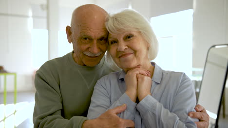 Senior-couple-hugging-and-looking-at-camera-in-a-studio