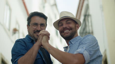 Front-view-of-gay-couple-looking-at-camera-and-joining-hands