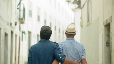 Back-view-of-happy-guy-couple-walking-down-lane-and-hugging