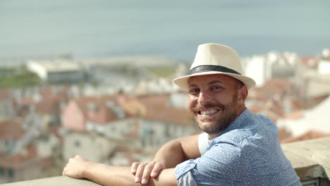 Slow-motion-of-happy-man-with-white-hat-looking-at-cityscape-from-view-point-and-then,-looks-to-the-camera-and-smiles