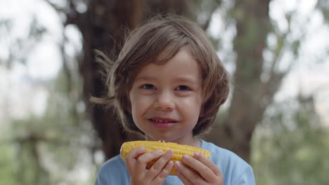 Close-up-of-happy-little-boy-eating-corn-cob-and-looking-at-the-camera