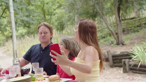 Happy-Caucasian-woman-taking-a-selfie-photo-with-her-family-during-a-picnic-in-the-forest