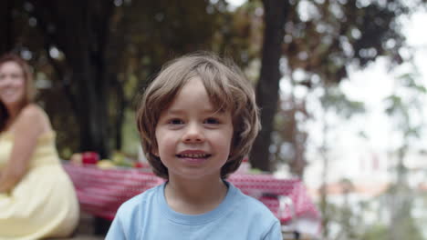 Medium-shot-of-cute-little-boy-posing-at-the-camera-during-a-family-picnic-in-the-forest