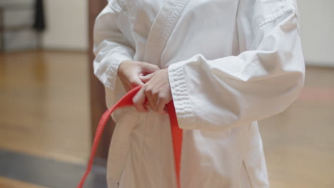 Front-view-of-woman-tying-orange-belt-on-kimono-in-gym