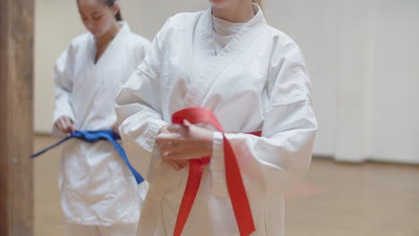 Front-view-of-focused-girls-tying-orange-and-blue-belts-on-kimonos