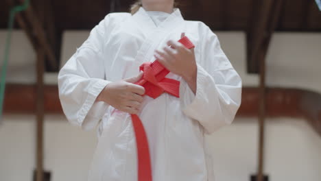 Medium-shot-of-girl-tying-orange-belt-on-kimono-in-practice-room