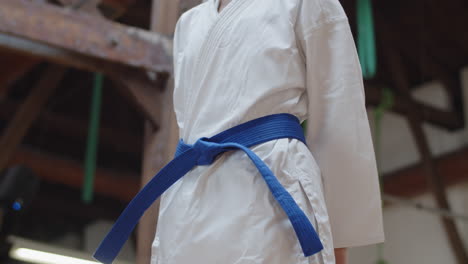 Plano-Medio-De-Mujer-Atando-Cinturón-Azul-En-Kimono-En-Sala-De-Práctica