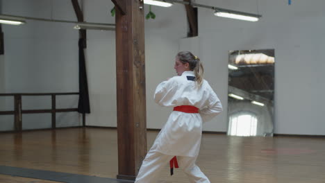 Tracking-shot-of-focused-girl-in-kimono-practicing-karate-in-gym