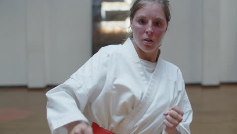 Tracking-shot-of-serious-girl-in-kimono-practicing-kicks-in-gym