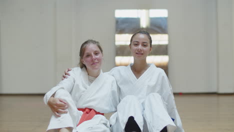 Front-view-of-happy-girls-in-kimonos-hugging-and-sitting-in-gym