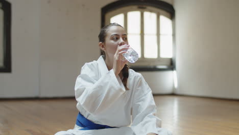 Vista-Frontal-De-Una-Chica-Alegre-Bebiendo-Agua-Después-Del-Entrenamiento-De-Karate