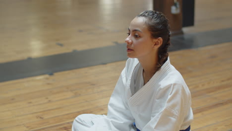 Side-view-of-karateka-sitting-on-floor-and-drinking-water