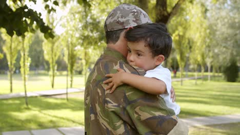 Padre-Militar-Feliz-Sosteniendo-A-Su-Hijo-En-Brazos-Al-Aire-Libre