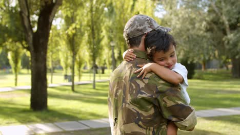 Happy-military-dad-holding-son-in-arms-outdoors