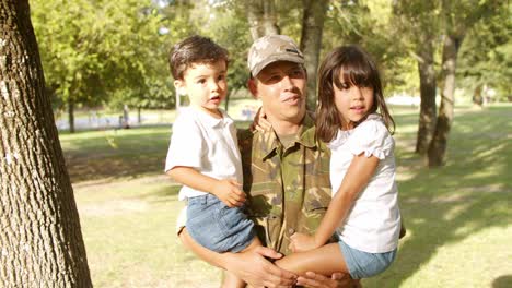 Happy-military-dad-holding-kids-in-arms-outdoors