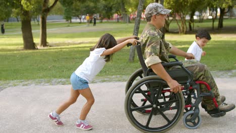 Kinder,-Die-Einem-Behinderten-Militärvater-Helfen,-Einen-Schweren-Rollstuhl-Zu-Rollen