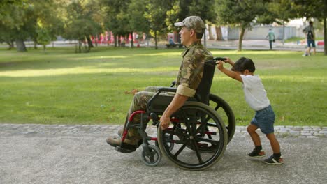 Chico-Lindo-Ayudando-A-Un-Padre-Militar-Discapacitado-A-Llevar-Una-Silla-De-Ruedas-Pesada