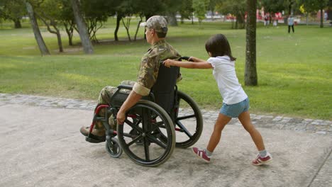 Daughter-kid-wheeling-wheelchair-with-disabled-dad