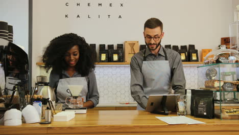 Caucasian-man-with-beard-and-african-american-young-female-barista-working-in-modern-coffee-shop