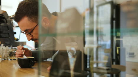 Side-view-of-caucasian-male-barista-with-beard-and-glasses-sniffing-the-fresh-coffee-in-a-coffee-shop